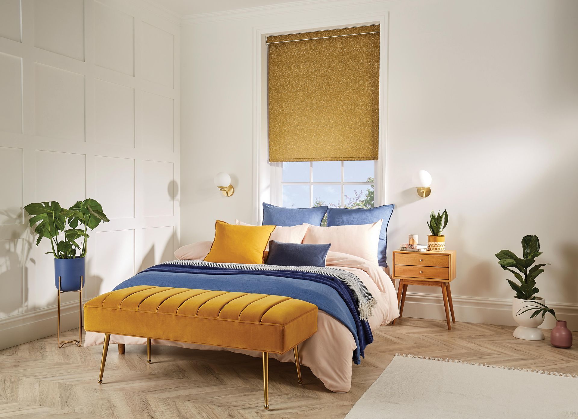 Bedroom with yellow accents, bed, bench, and window shade; white walls, wooden nightstand, plants.