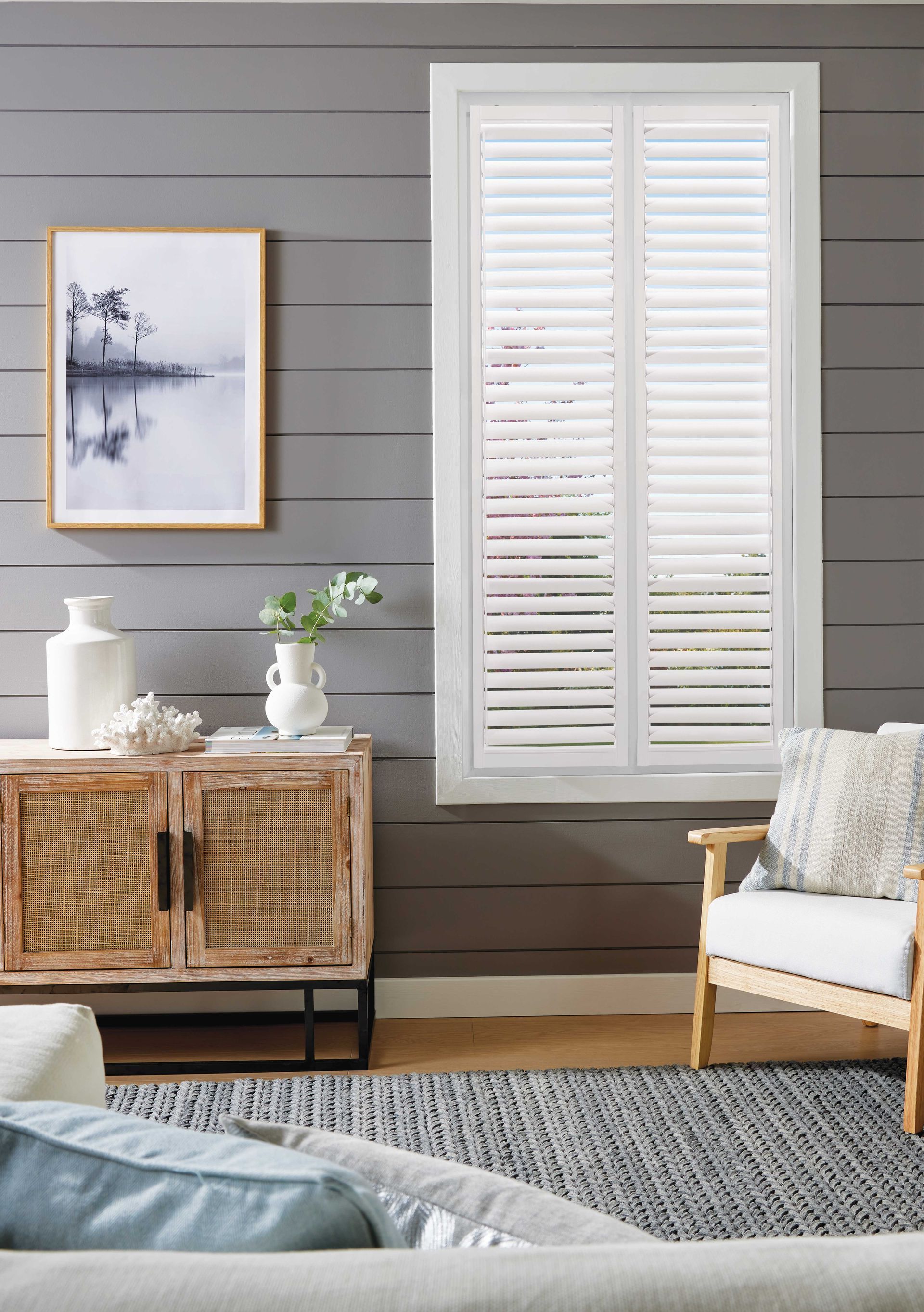 Living room with a wooden cabinet, artwork, white shutters, and a cozy armchair.