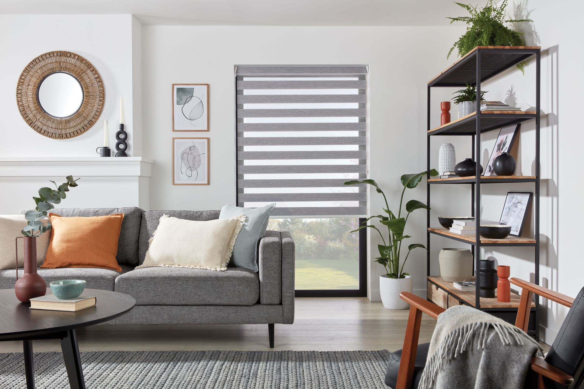 Living room with gray sofa, window blinds, shelving unit, and decorative items.