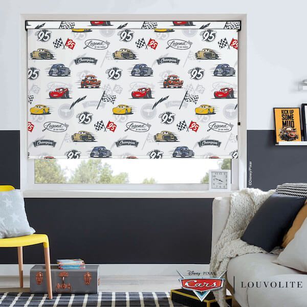 A window with a car-themed blind, a sofa with pillows, and a yellow chair.