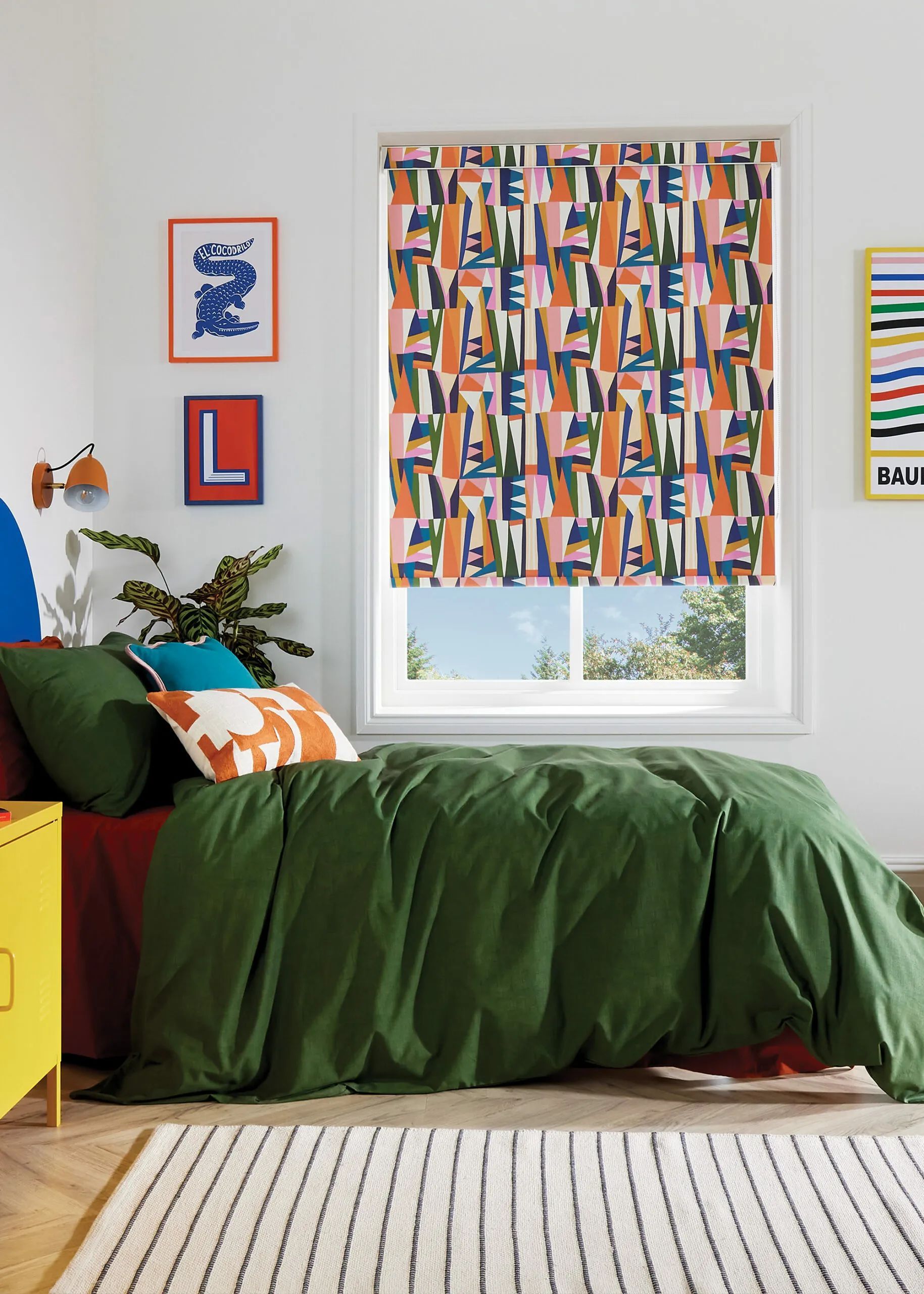 Bedroom with green bedding, patterned window blind, artwork, and a yellow bedside table.