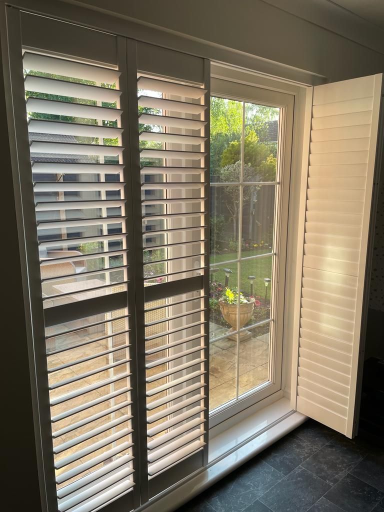 White shuttered window, partially open, revealing a sunny outdoor view.