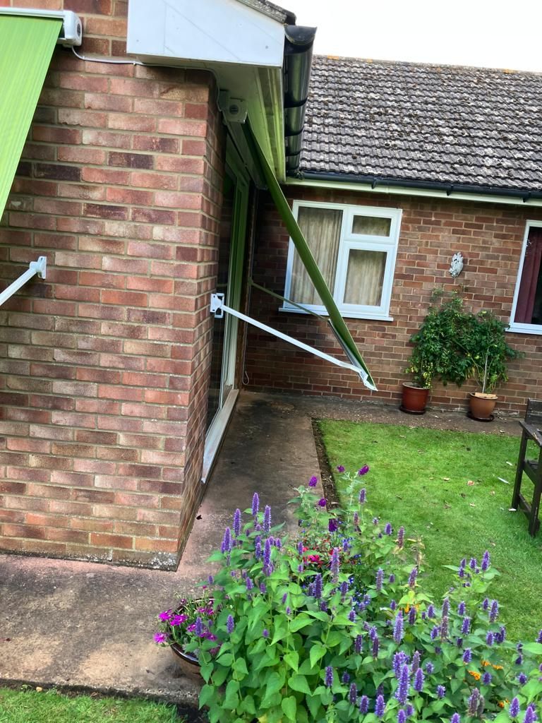 Green awning attached to a brick building, extending over a doorway. Small garden in foreground.