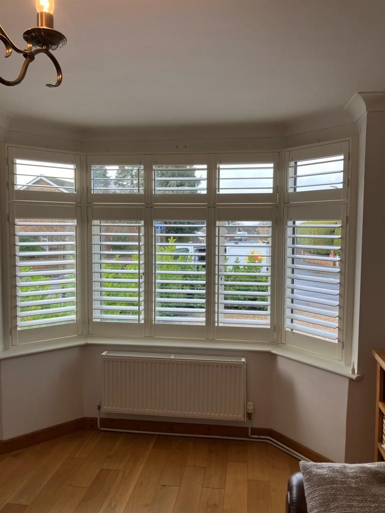 Bay window with white shutters, a radiator, and hardwood flooring.
