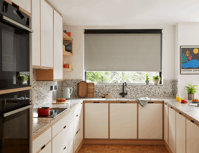 Modern kitchen with white cabinets, speckled countertops, black sink, and window with closed blinds.
