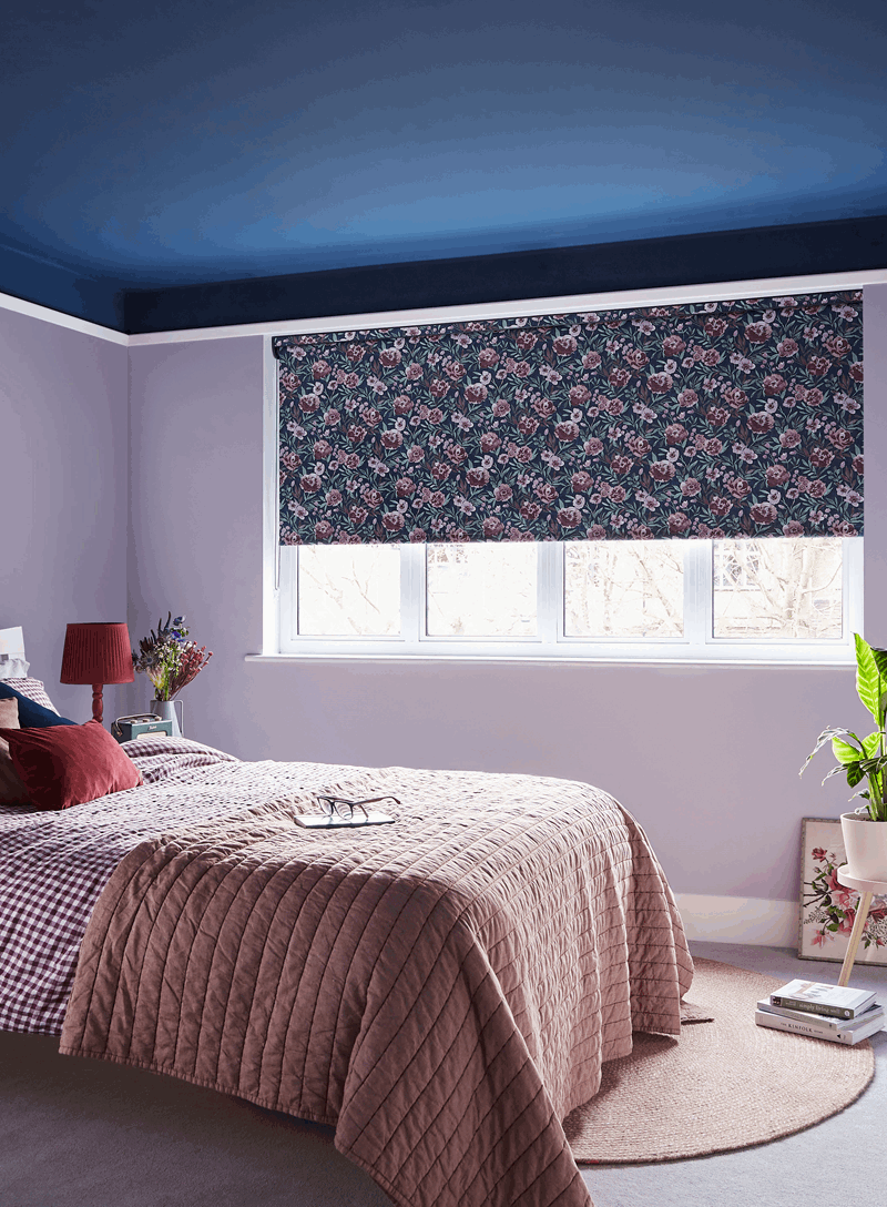 Bedroom with lilac walls, a blue ceiling, floral blinds, and a bed with a pink quilt.