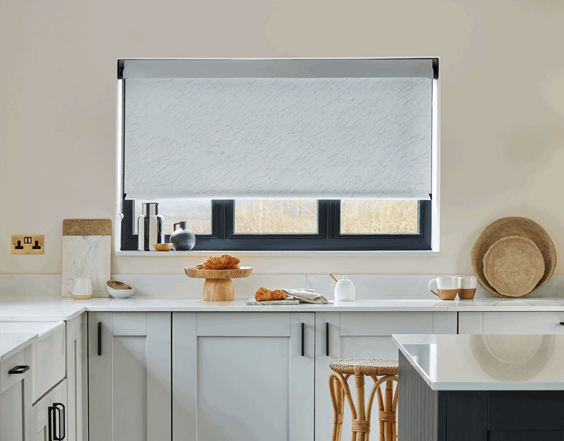 Kitchen with a window partially covered by a light-colored roller blind. Counter and cabinets in front.