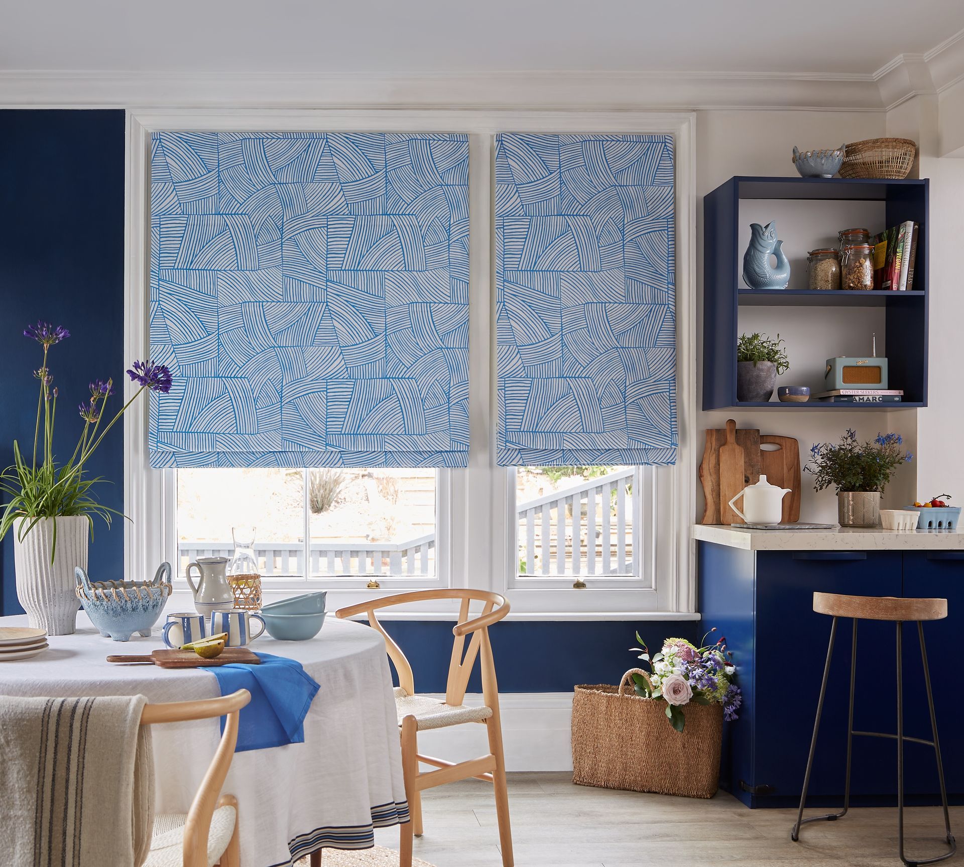 Kitchen with blue walls and patterned blinds, table set, and wooden chair.