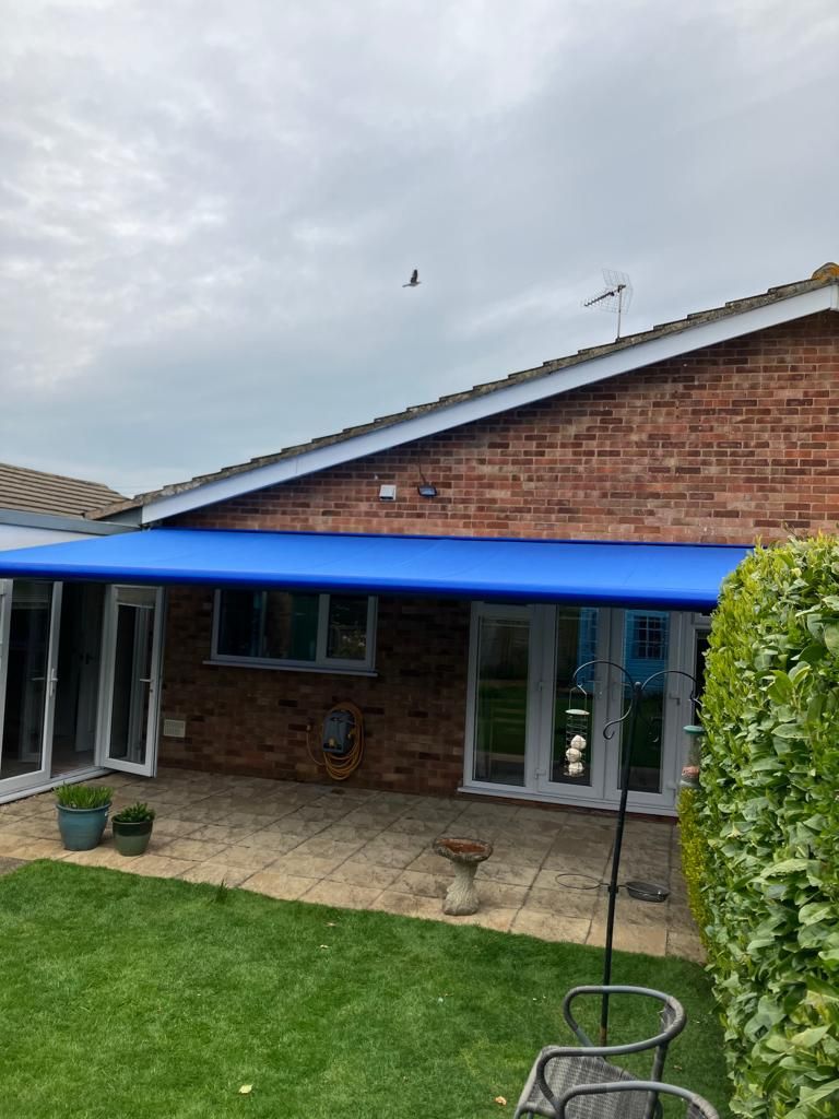 Blue awning over a brick building with a patio and yard on an overcast day.