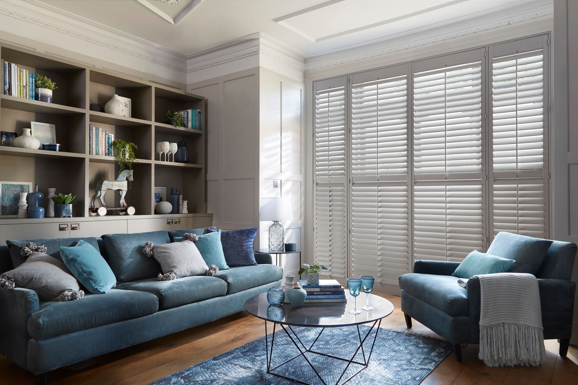 Living room with blue sofa, armchair, and bookshelf; white shutters on window.