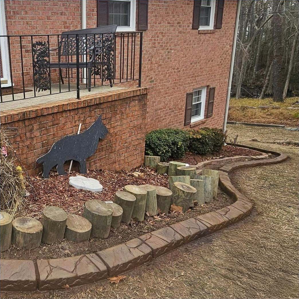 A brick house with a raised porch, a metal dog silhouette in the garden, and a curved concrete edging bordering mulch.