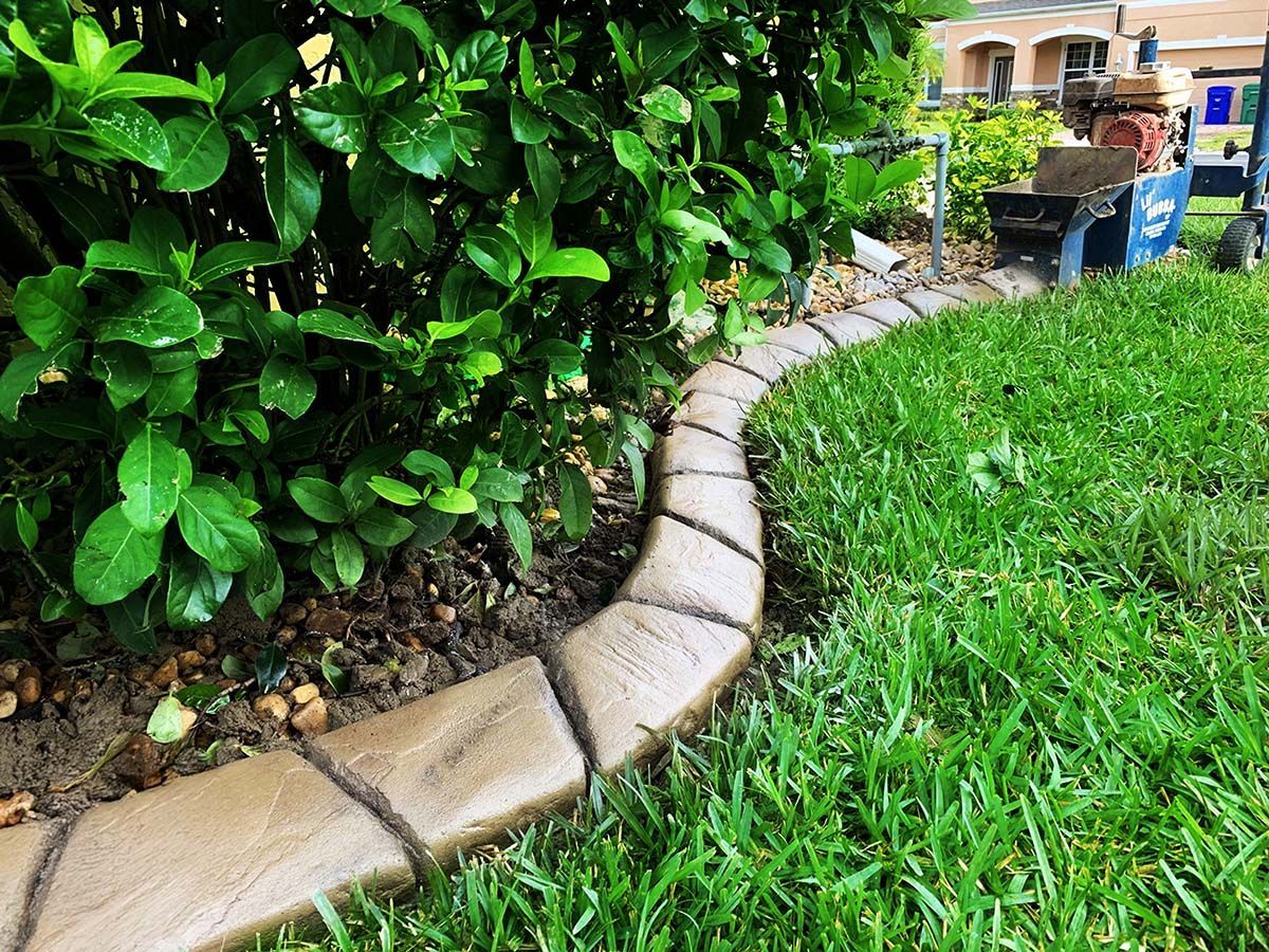 Brown decorative concrete border edging a green lawn next to lush green foliage.