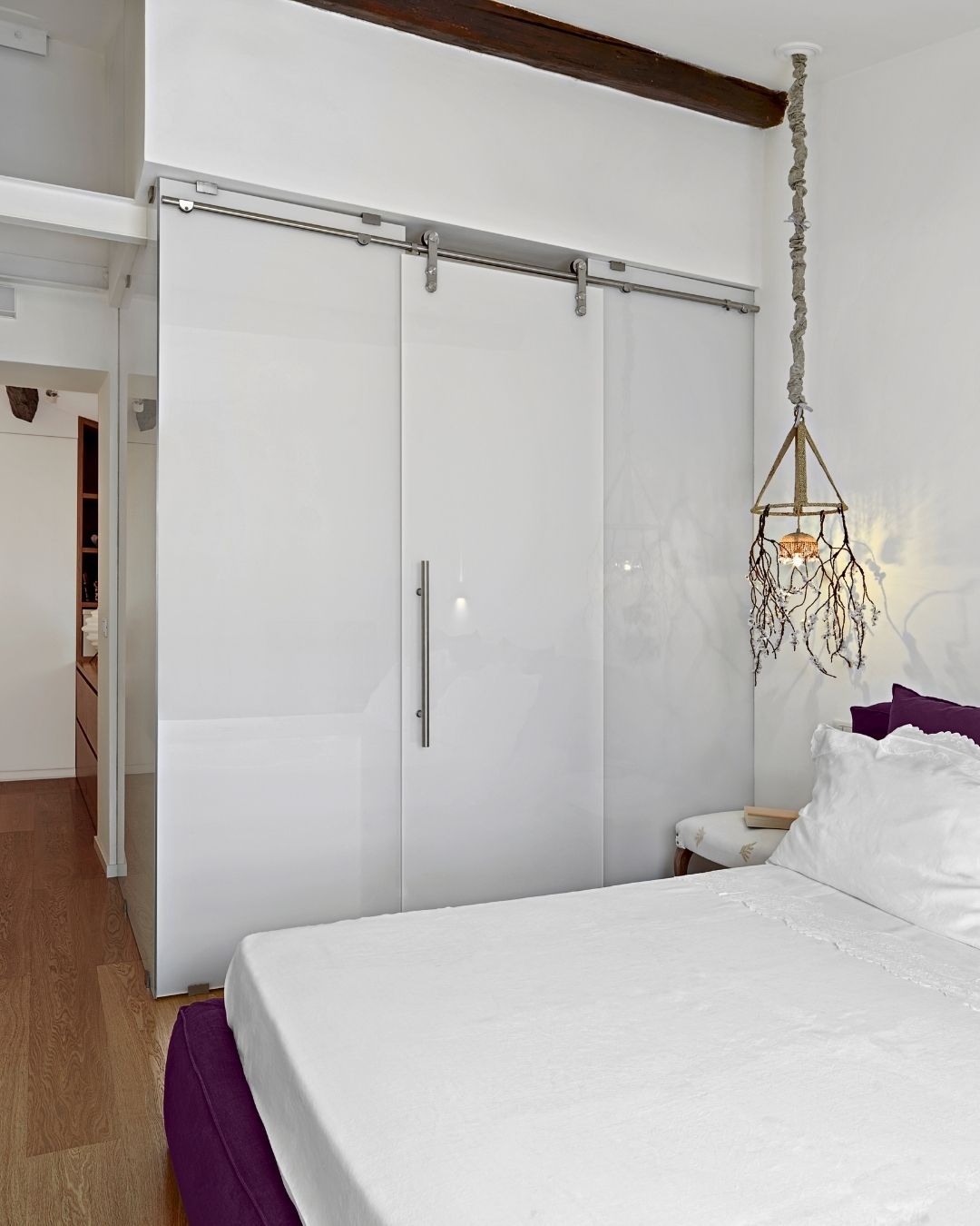 A bedroom with white sliding-door wardrobes, a white bed with purple accents, and a unique hanging lantern.
