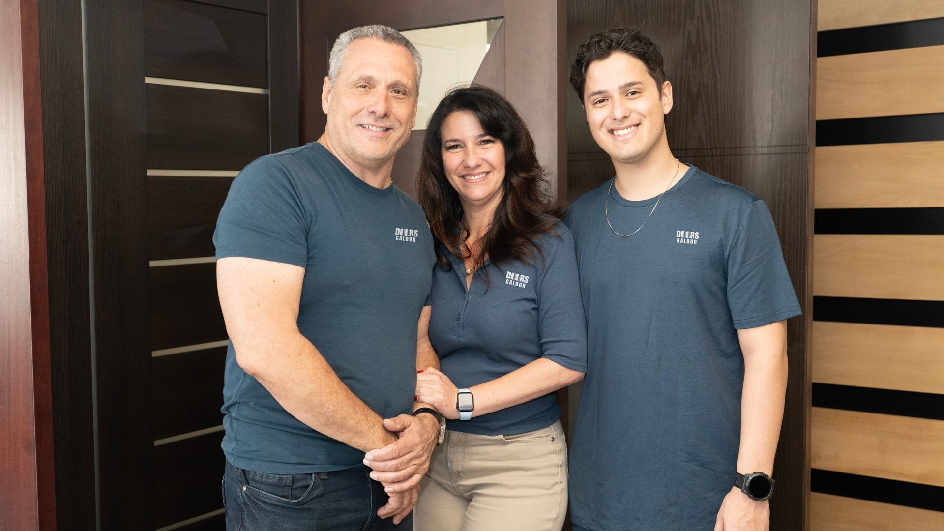 Three people standing together indoors, smiling and wearing matching dark shirts.
