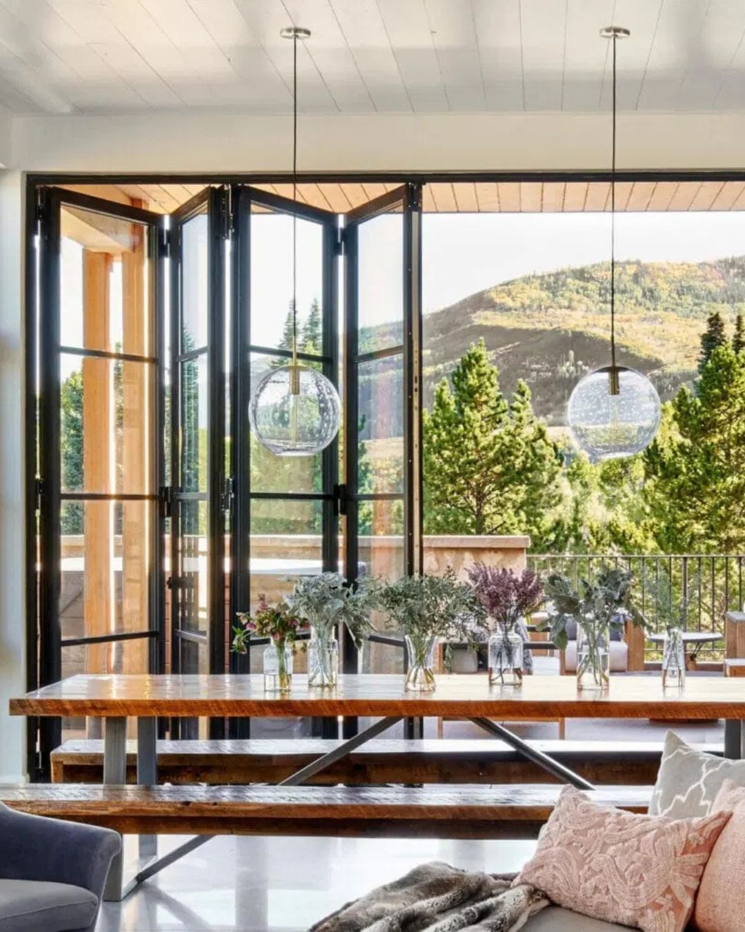Modern living room with large open windows, glass doors, and a mountain view beyond the terrace.