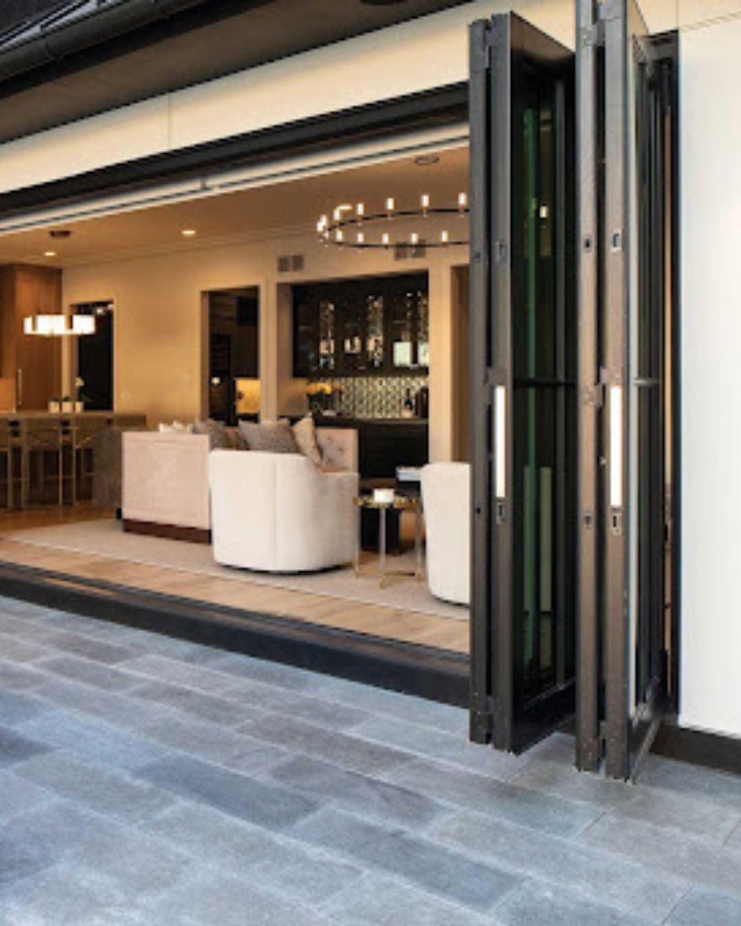 Open storefront with folded glass doors, showing a modern café interior with white chairs and warm lighting.