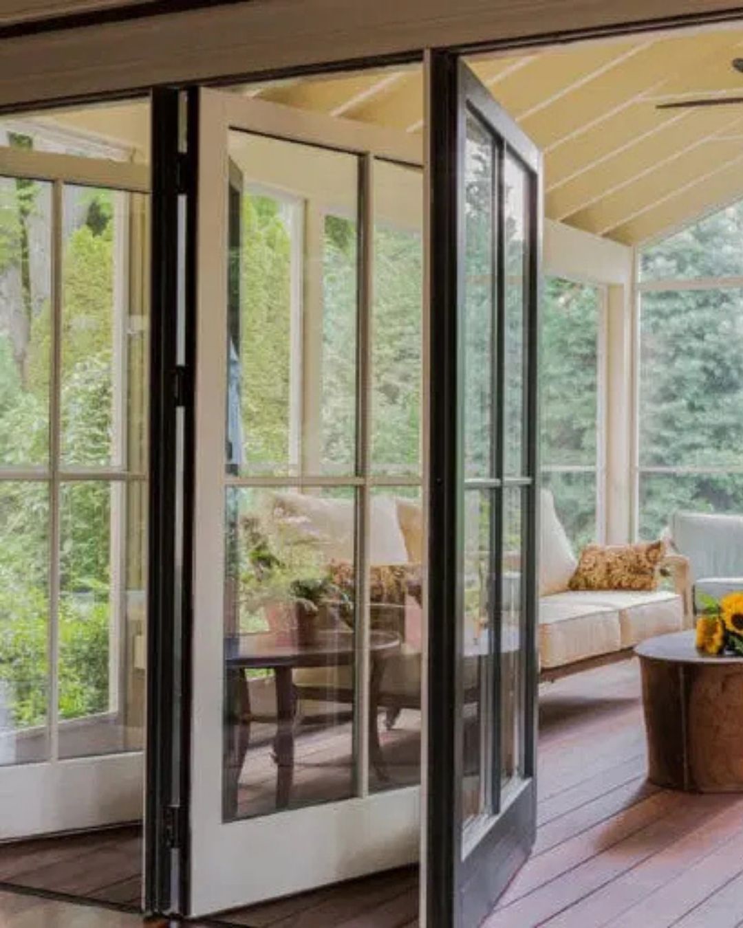 Open glass doors to a bright screened porch with a sofa, chair, and wood deck.
