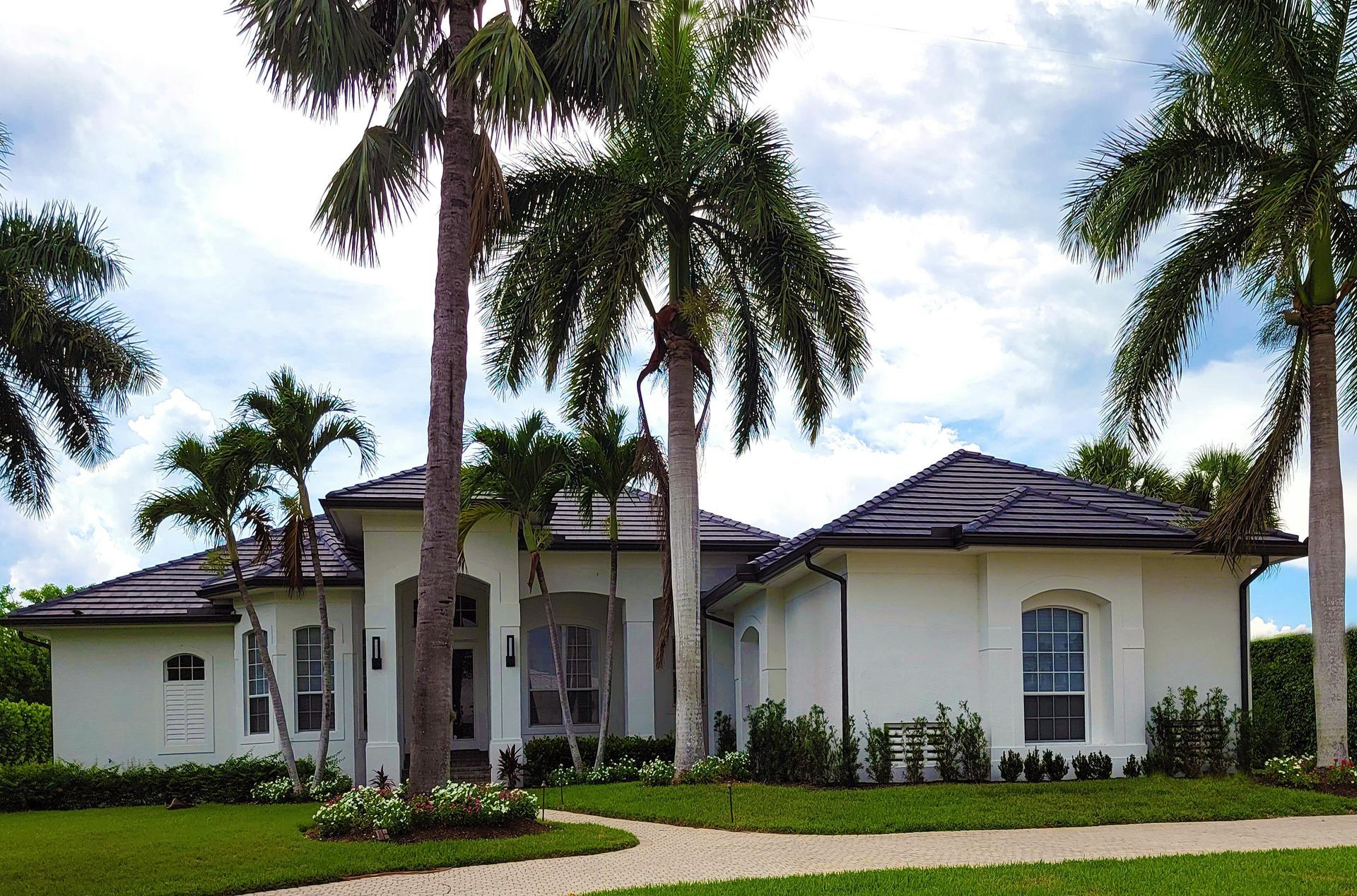 Single-story white house with dark roof and palm trees in a landscaped yard