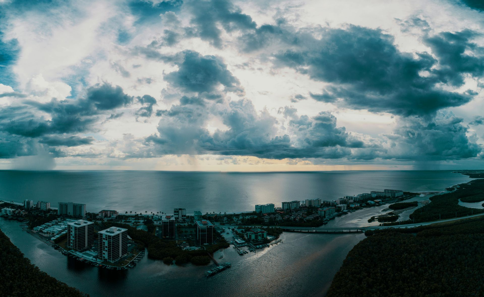 Panoramic coastal harbor at dusk with calm water, cloudy sky, and dark buildings on islands