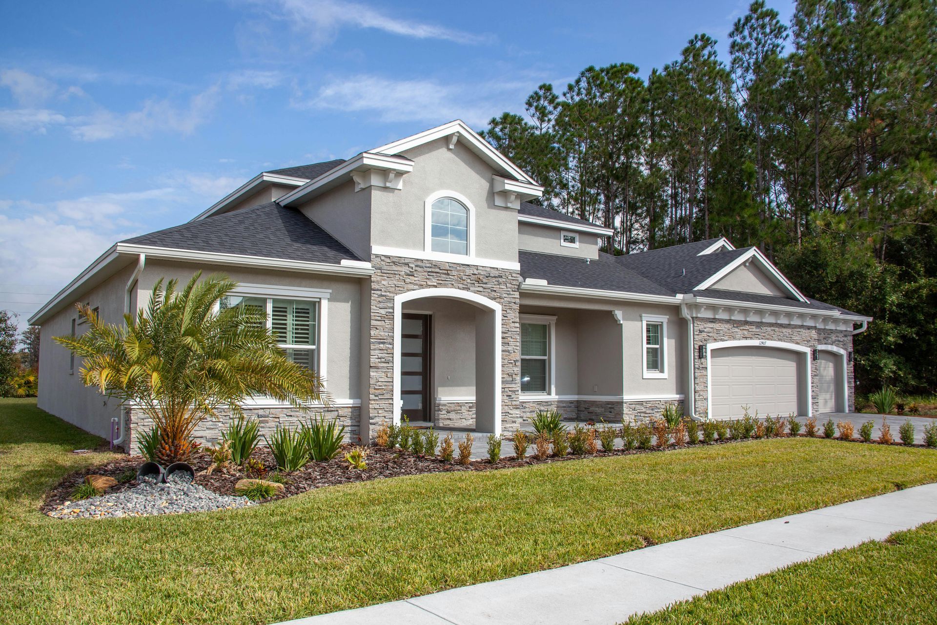 Gray suburban house with stone accents, front lawn, and palm tree by a sidewalk