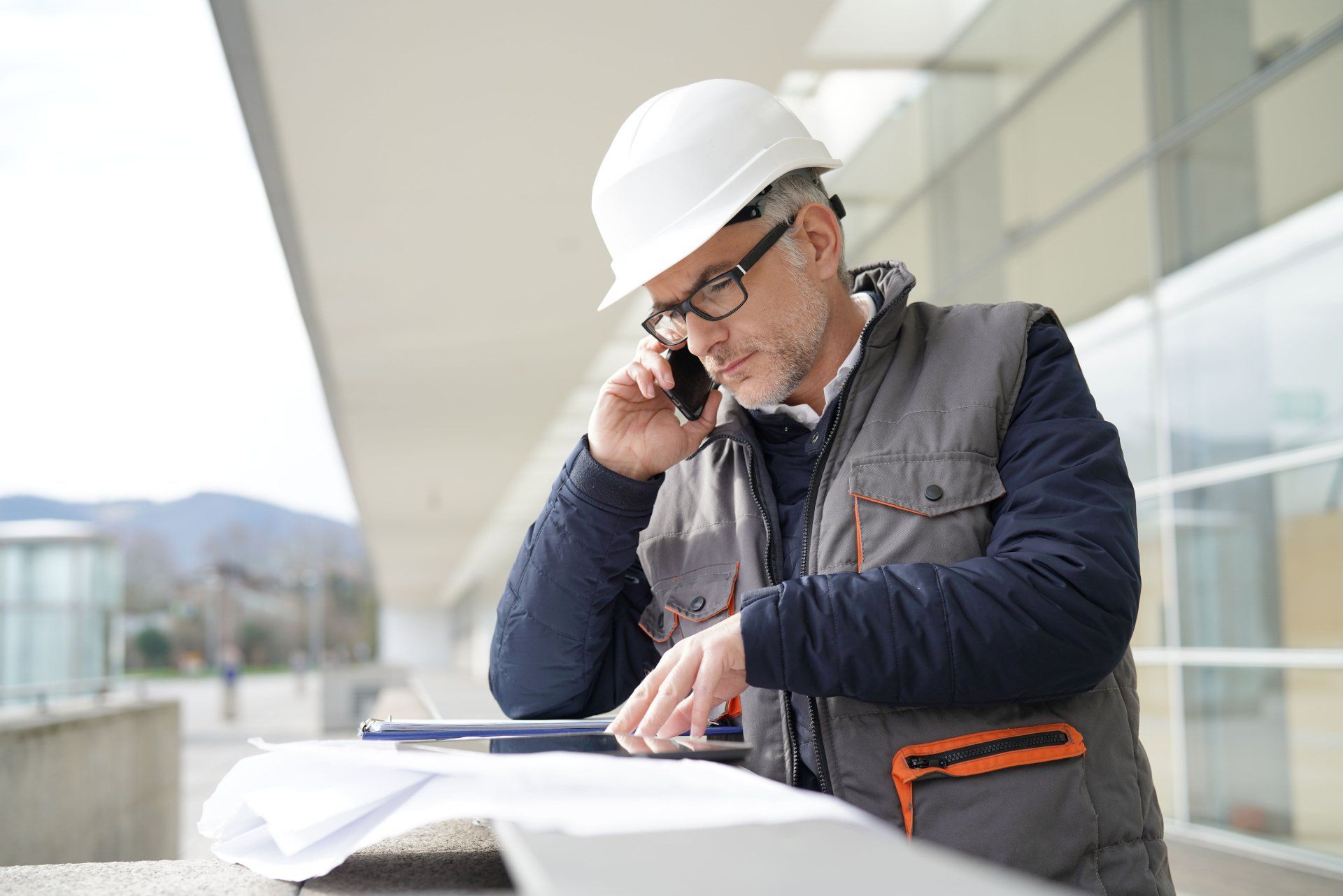 Un ouvrier du bâtiment parle sur un téléphone portable tout en regardant un plan.