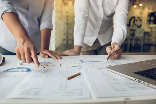 Deux hommes regardent un plan sur une table.