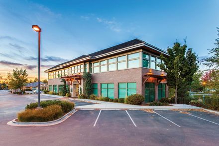 Modern two-story office building with brick and glass facade, parking lot, and a streetlamp at dusk