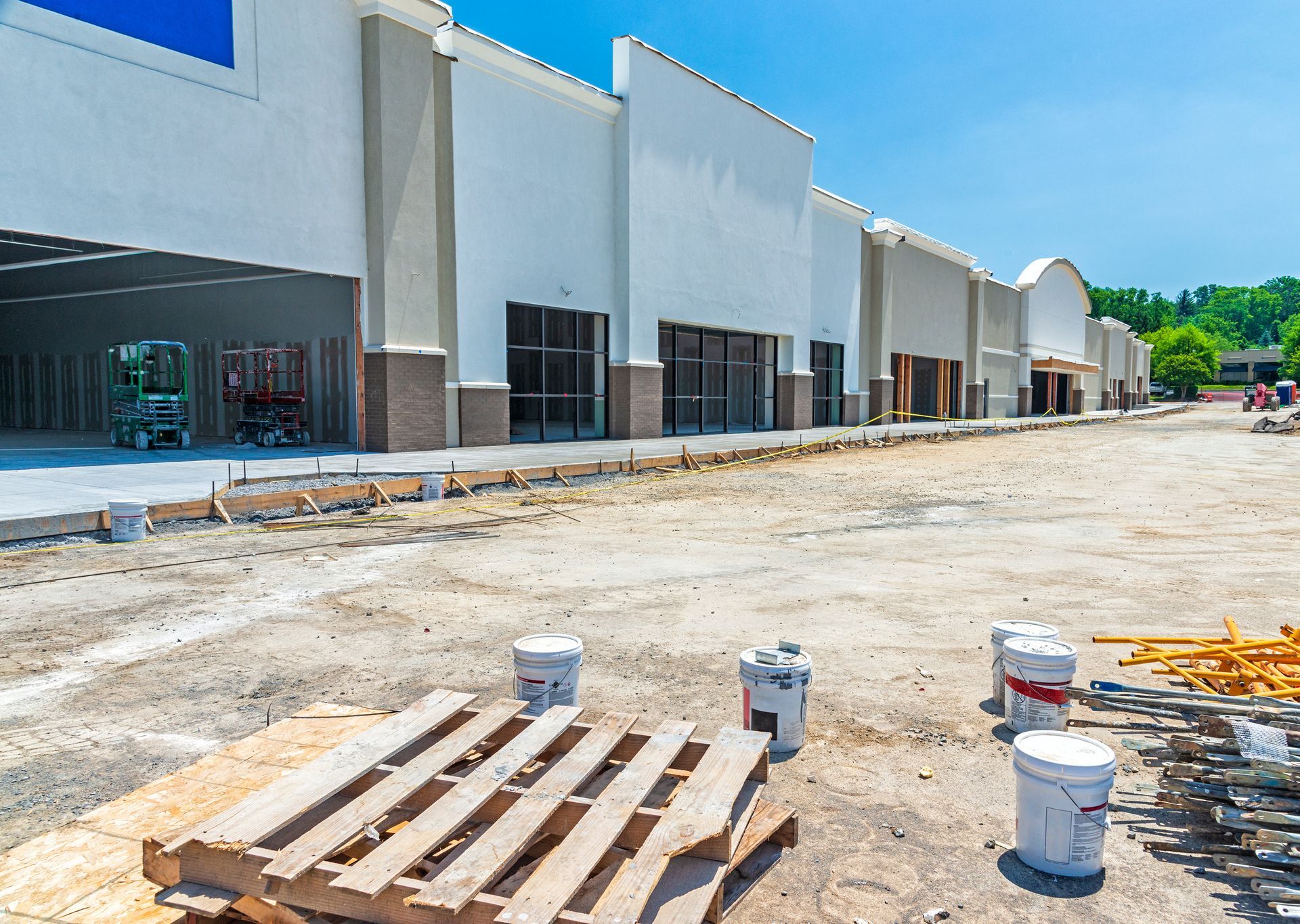New commercial building under construction with pallets, paint buckets, and dirt lot in front