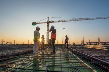 Construction workers on a rebar deck at sunset with a tower crane overhead