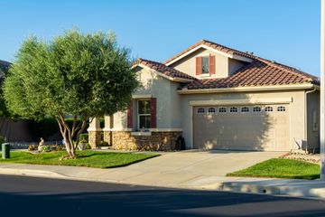 Suburban house with a two-car garage, stone accents, and a leafy front yard under a clear blue sky