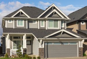 Two-story gray suburban house with stone accents, white trim, and a double garage under a blue sky