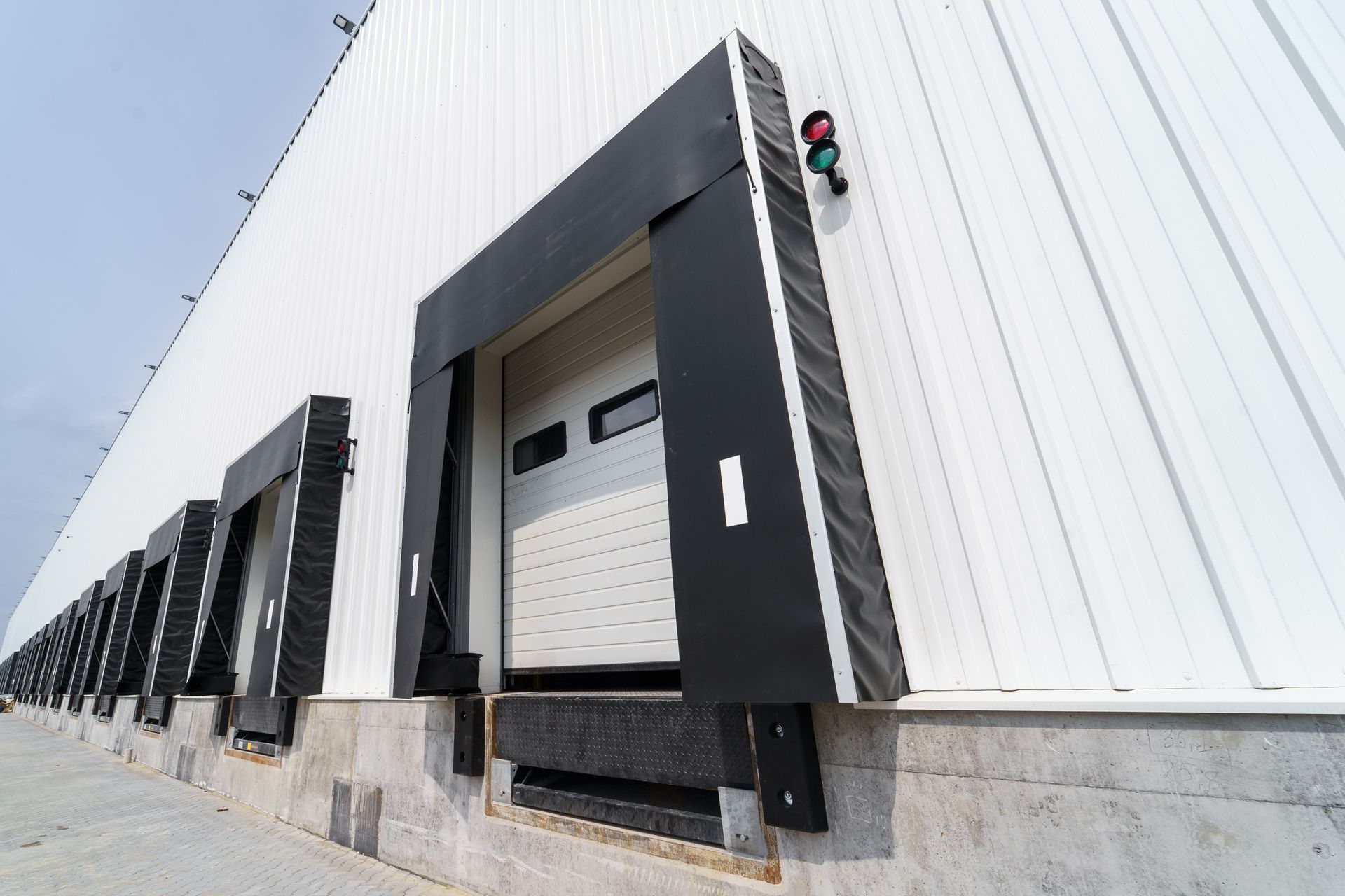 Loading dock on a white industrial building with black doors and a red-green signal light