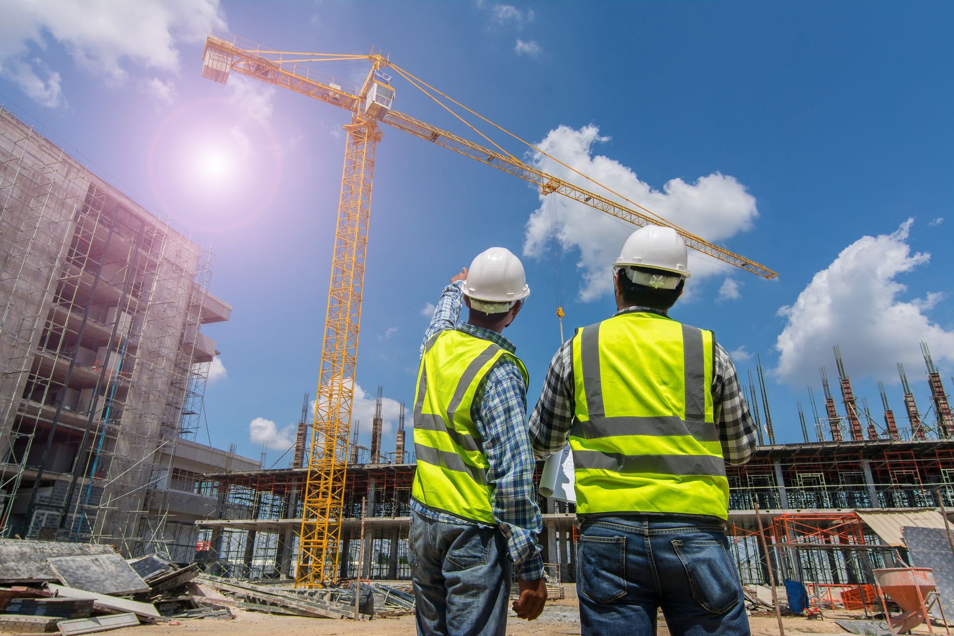 Two construction workers in hard hats and neon vests at a building site with cranes and scaffolding