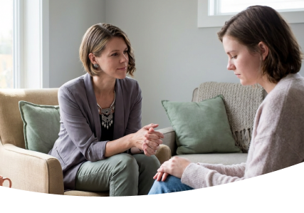 Two women seated on a couch, talking quietly in a bright living room