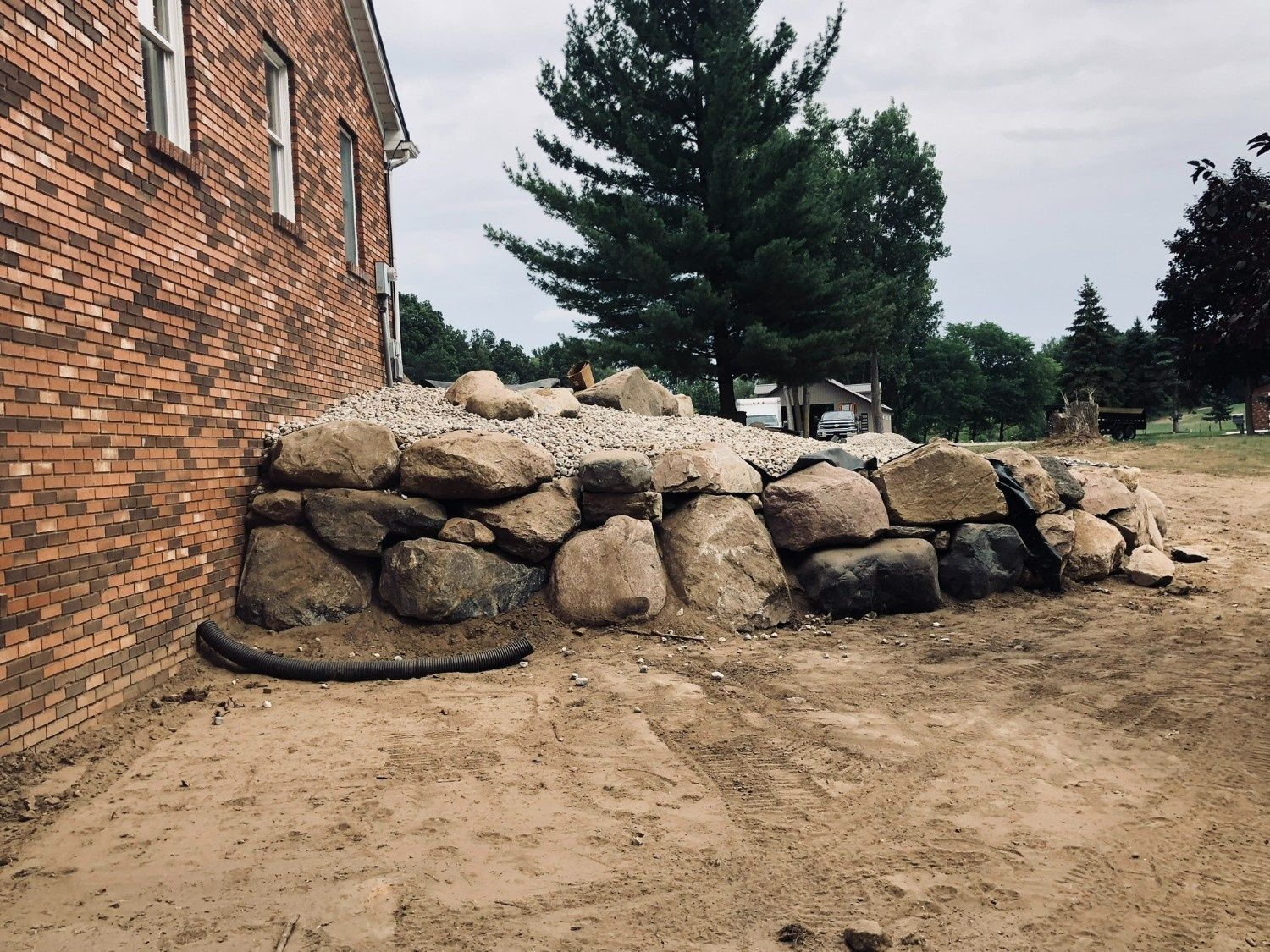 Brick building beside a stacked rock retaining wall and sandy ground under a cloudy sky