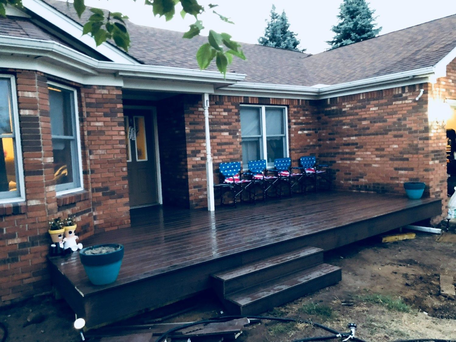 Brick house back patio with wet wooden deck, potted flowers, and open doorway