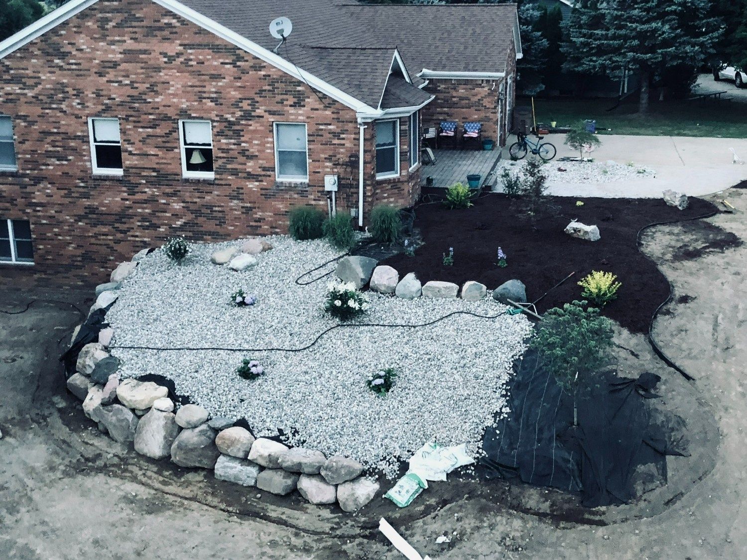 Landscaped yard with white gravel, large rocks, and dark mulch beside a brick house
