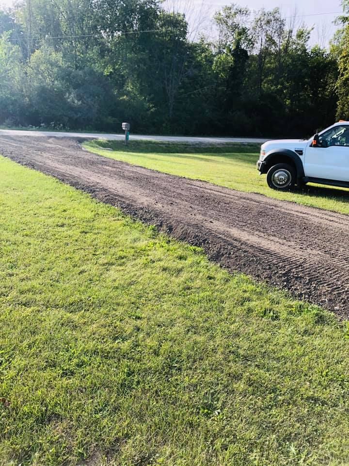 White pickup truck on a dirt road beside a grassy field and trees in bright sunlight