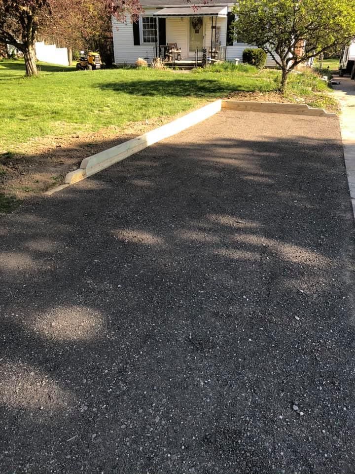 Driveway leading to a small white house with a front porch and green lawn.