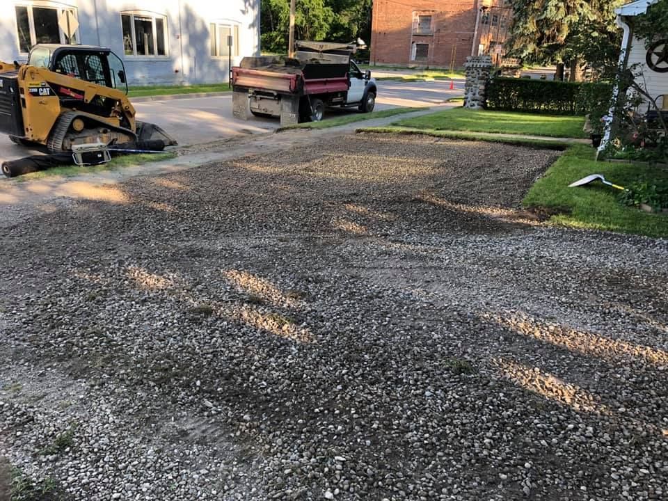 Gravel driveway under construction with a skid steer and dump truck parked beside it