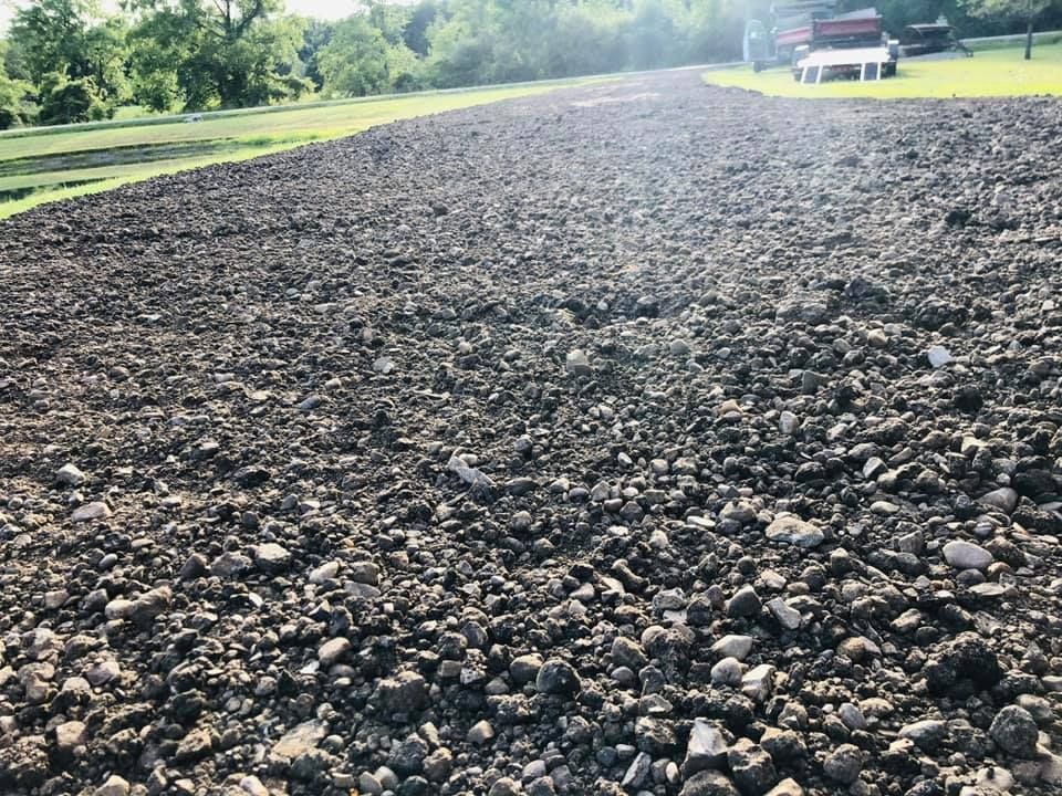 Gravel road stretching into the distance with trees and a red building in the background