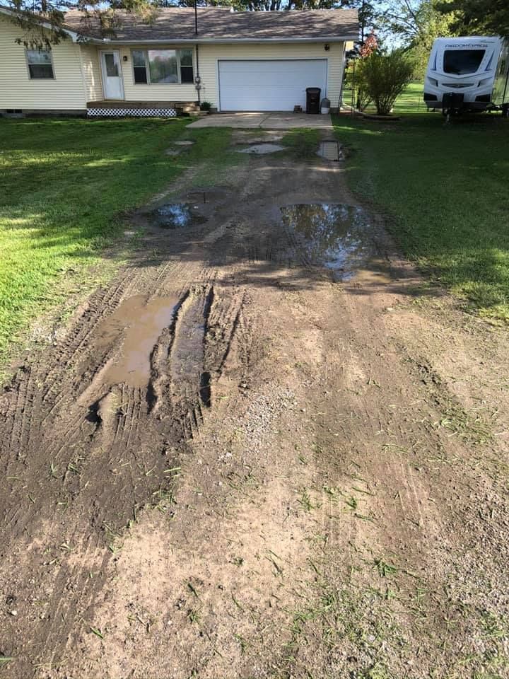 Muddy, rutted driveway leading to a suburban house with a garage, with a camper parked on the right.