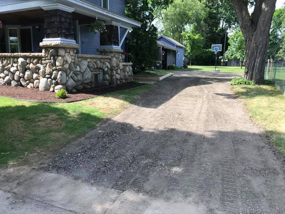 Gravel driveway beside a stone house, lined with trees on a sunny day