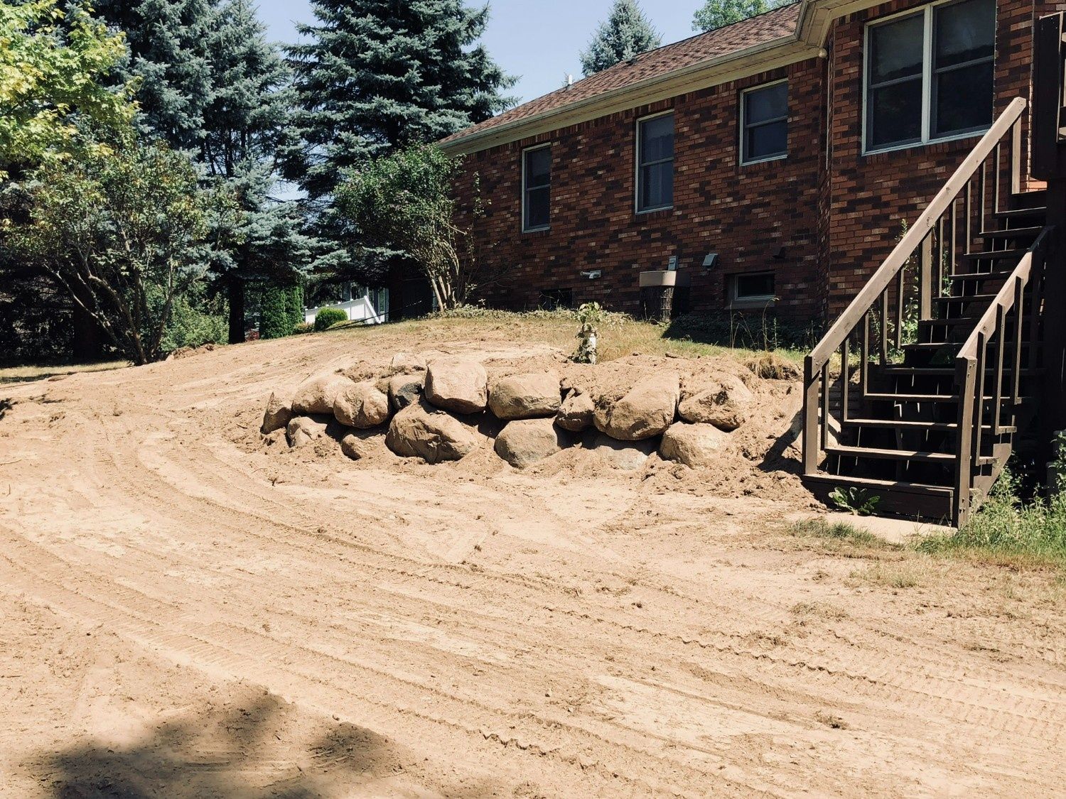 Brick house with exterior stairs beside a dirt slope and a damaged retaining edge