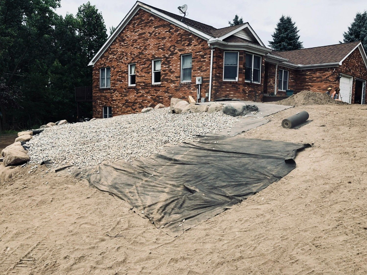 Brick house behind a large sand pile and gravel spread across a construction site