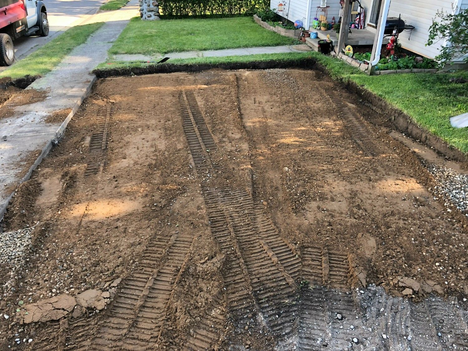 Freshly graded dirt driveway under construction beside a lawn and sidewalk