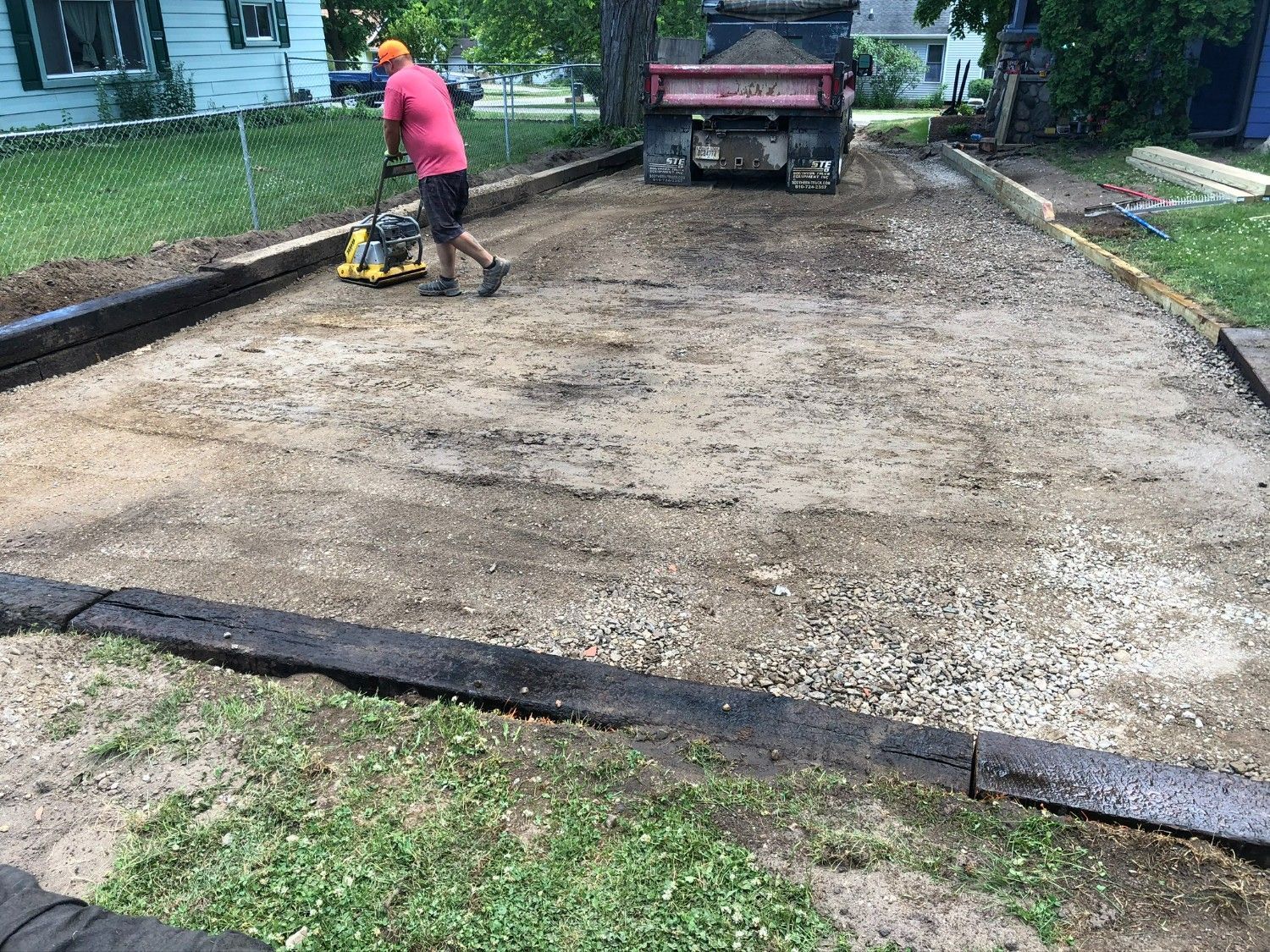 Worker compacting a freshly graded gravel driveway with a plate compactor near a pickup truck