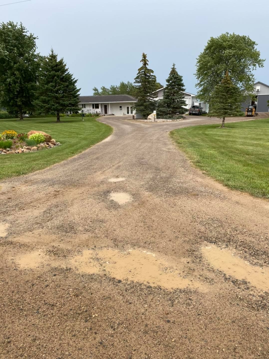 Gravel driveway leading to a house with trees and lawn on a cloudy day