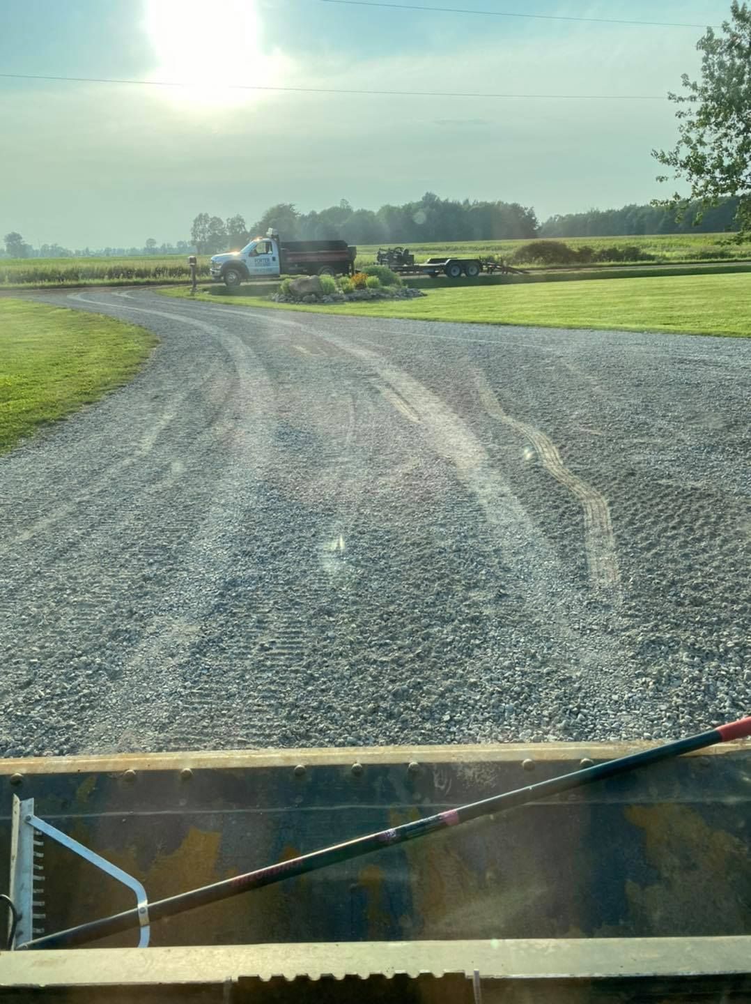 Gravel road curving through green fields under a bright sky, seen from inside a vehicle.