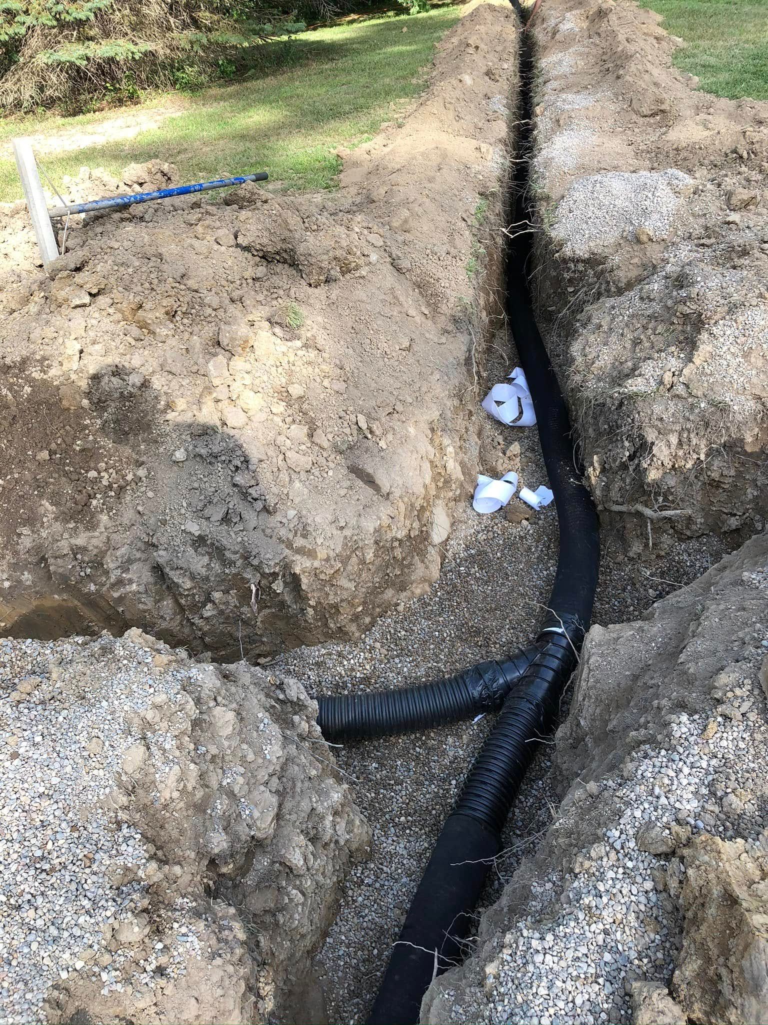 Trenched ground with a black corrugated pipe laid in a narrow ditch outdoors